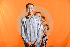 Four children stand in a row on a yellow background, the younger ones look out for the older ones