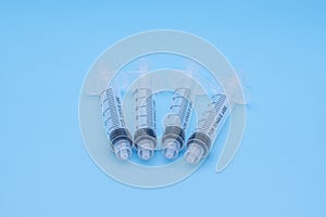 Four clear plastic 5ml syringes isolated against a blue background
