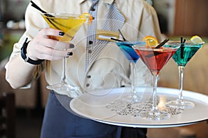 Four colored cocktails on a tray in the hands of the waiter. Yellow, blue, green, red. Waiter raises a yellow