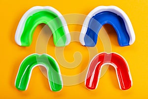 Four colored mouthguards on a yellow background, two adults and two children`s mouthguards, tooth protection, the concept of