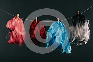 Four colorful wigs hanging on rope isolated