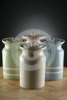 Four colourful ceramic canisters on timber bench with grey spot on background
