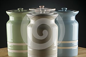 Four colourful ceramic canisters on timber bench with grey spot on background