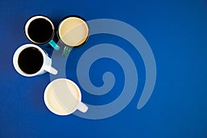 Four cups with different kinds of coffee on a blue background with empty space, minimalistic composition with hot beverages, top