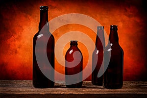 Four dark brown glass beer bottles on a barn wood table in front of an orange background