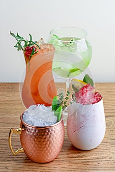 Four different assorted cocktail drinks made with alcohol and fruit served in unique cups and glasses on wooden table