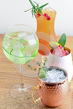 Four different assorted cocktail drinks made with alcohol and fruit served in unique cups and glasses on wooden table