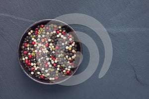 Four different kinds of peppercorns in clay bowl on stone background, copy space, top view