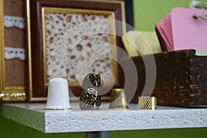 Four different thimbles on a wooden shelf on the background of knitted pictures and labels for clothes