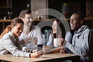 Four diverse friends having fun use gadget sitting in cafe