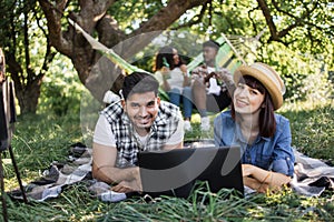 Four diverse friends using laptop on picnic at garden