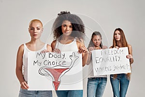 Four diverse women looking at camera while holding, standing with banners in their hands isolated over grey background