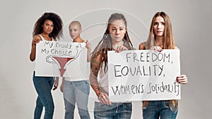 Four diverse women looking at camera while holding, standing with banners in their hands isolated over grey background