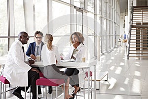 Four doctors talking at a table in a modern hospital lobby