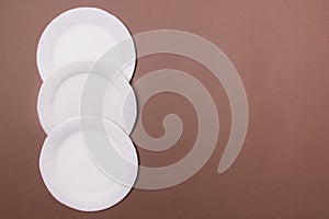 Four eco-friendly white paper plates lie on brown background with copy space. top view. close-up