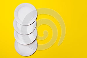 Four eco-friendly white paper plates lie on yellow background with copy space. top view. close-up