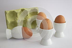 Four eggs in white eggs cups, on white isolated background with yellow carton egg box.