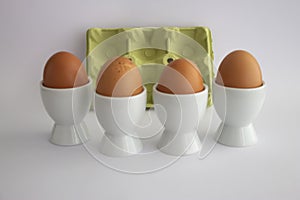 Four eggs in white eggs cups, on white isolated background with yellow carton egg box.