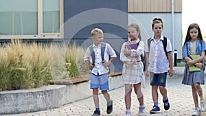 Four elementary school students, two boys and two girls, are walking around the school yard. The children are talking