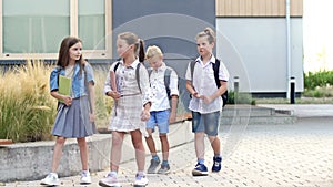 Four elementary school students, two boys and two girls, are walking around the school yard. The children are talking