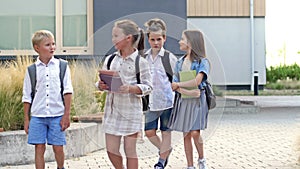 Four elementary school students, two boys and two girls, are walking around the school yard. The children are talking