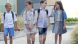 Four elementary school students, two boys and two girls, are walking around the school yard. The children are talking