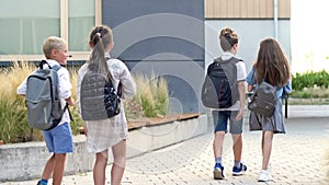 Four elementary school students, two boys and two girls, are walking around the school yard. The children are talking