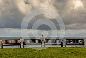 Four empty, wooden benches looking out to sea by the North Pier of the mouth of the River Tyne on a cloudy day