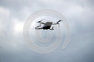Four engine drone with camera flying in the grey cloudy sky closeup
