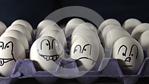 Four faces drawn on the white eggs on the tray