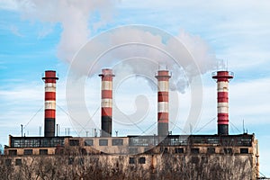 Four factory chimneys emit puffs of smoke against the blue sky.