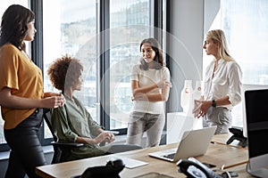 Four female colleagues in discussion at a desk in a creative office, three quarter length photo