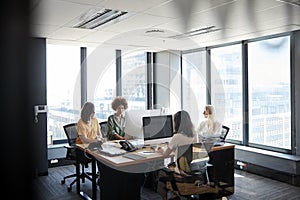 Four female creative colleagues working together in an office, seen through glass wall