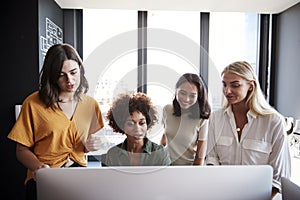 Four female creatives working around a computer monitor in an office, front view, close up