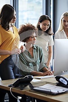 Four female creatives working around a computer monitor in an office, side view, vertical, close up