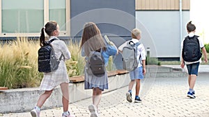 Four first graders, two boys and two girls, are walking around the school yard. Back to school.