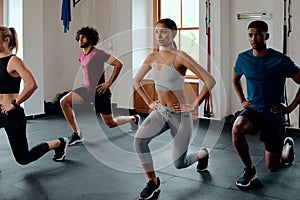 Four focused multiracial young adults in sportswear doing lunges at the gym