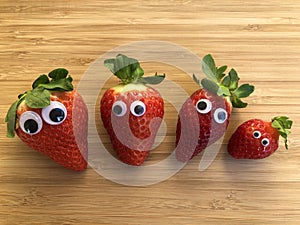 Four fresh red strawberries with googly eyes