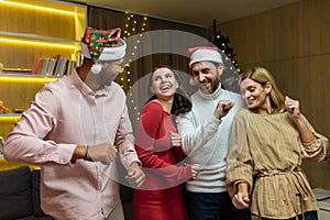 Four friends celebrating dancing on christmas near christmas tree at home, diverse group of guests at house party having