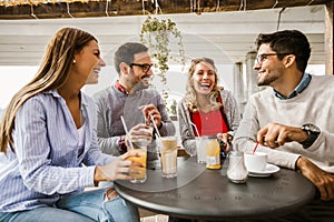 Four friends having fun a coffee together. Two women and two men at cafe talking laughing and enjoying their time