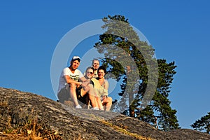 Four friends sitting on edge of mountain at sunset