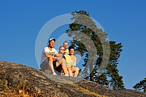 Four friends sitting on edge of mountain at sunset