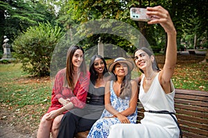 Four friends are sitting on a patch in a public park and taking a selfie together. Diversity and friendship between women