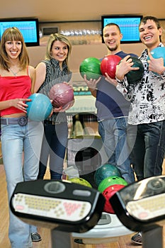 Four friends stand near tenpin bowling with balls