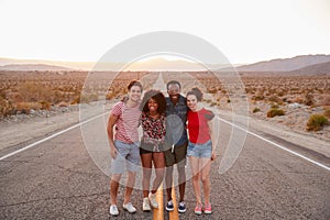 Four friends standing on a desert highway smiling to camera