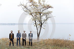 Four gangsters stand in the fall. Three of them crossed their arms, one of them was holding a hat. Retro. Outdoors.