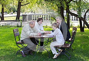 Four generations of men sitting at a wooden table in a park, laughing and talking