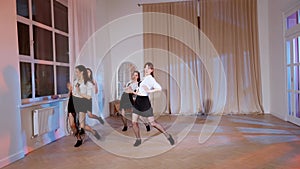 Four girls in black skirts and white shirts are dancing indoors.