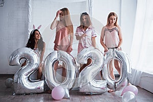 Four girls in pink and white clothes stands with silver colored balloons. Conception of happy new year