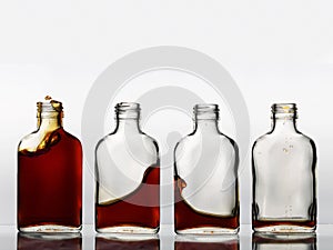 Four glass bottles in a row with different amount of brown color beverage in each, that churning and spills out.